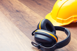 A yellow hard hat and hearing protection on hardwood floor