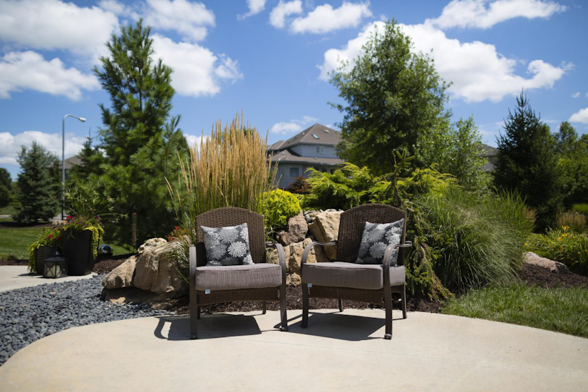 A hardscaped area with two chairs surrounded by rock, grass, and ornamental grass landscaping