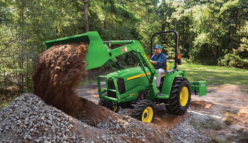 John Deere 3032E compact tractor dumping a bucket of dirt and gravel onto a pile