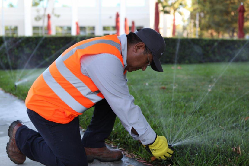 A landscaper wearing an orange safety vest while irrigation sprinklers are set